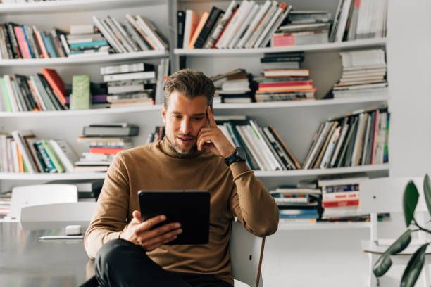 istock Handsome Young Teacher Using a Digital Tablet at the Library, Preparing to Give a Lecture 1363123434