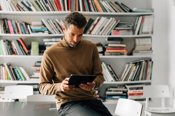 istock Handsome Young Teacher Using a Digital Tablet at the Library, Preparing to Give a Lecture 1363123435