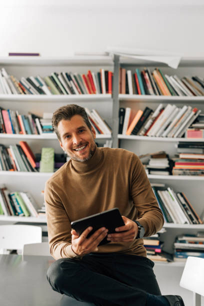 istock Handsome Young Teacher Using a Digital Tablet at the Library, Preparing to Give a Lecture 1363123436