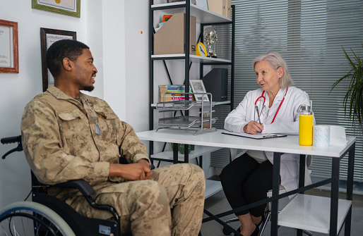 Soldier in a wheelchair. He is discussing injury and trauma with a military doctor or counselor during an appointment
