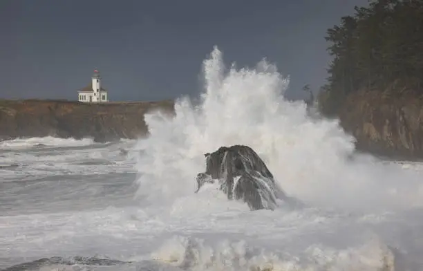 A large wave crashes into the rocks in front of the Cape Arago Lighthouse.  Located on Cape Arago near Charlestown, Oregon.