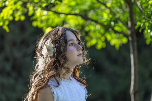 Close-up shot of young girl looking up pensively wearing communion dress next to sunny tree. Madrid, Spain Madrid Spain. May 5, 2018. Close-up shot of young girl looking up pensively wearing communion dress next to sunny tree 9 stock pictures, royalty-free photos & images