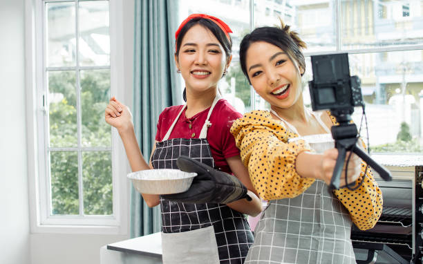 istock Two beautiful Asian women cooking food, making bread for breakfast and bakery while using tablet, streaming live video clip or taking selfie photo together with happiness and fun in kitchen at home. 1363132491