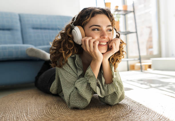 pretty curly-haired woman lying on the floor at home listening to music happy smiling relaxed - lying down women laptop freedom imagens e fotografias de stock