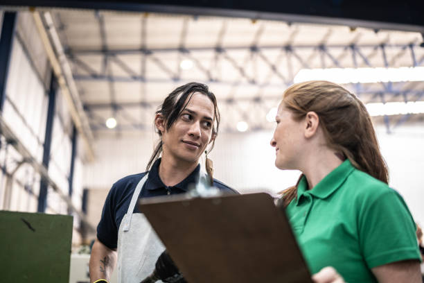 istock Inspector talking to non-binary production line worker in a factory 1363134742