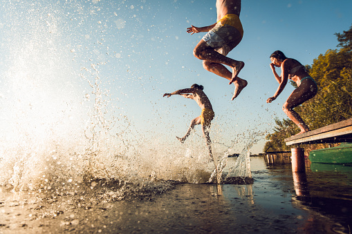 Young friends having fun enjoying a summer day swimming and jumping at the lake.