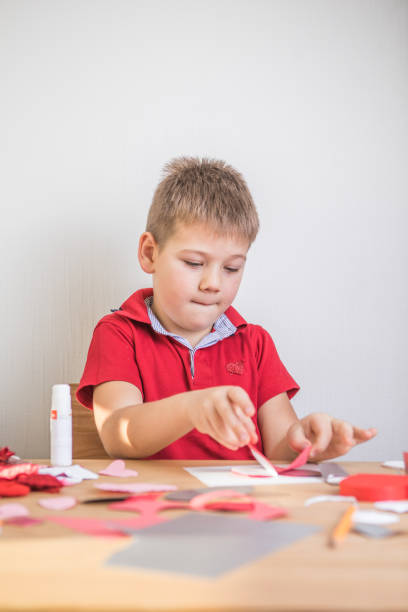 DIY holiday card with red paper heart, symbol of love. Kid boy makes Mother's Day, Valentine's Day, greeting card. Hobby, children art concept, gift with your own hands, DIY Ideas for children tarjeta navideña de bricolaje con corazón de papel rojo, símbolo de amor. niño hace el día de la madre, el día de san valentín, la tarjeta de felicitación. hobby, concepto de arte para niños, regalo con tus propias manos, ideas de bricolaje para n