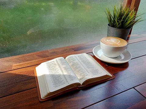 Bible on wooden table with morning light through steam window in winter.Concept Love study God word in coffee time,Christian believe holy cross,faith,hope,forgiveness,praying worship key for new day.