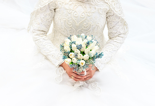 The bride holds her bridal bouquet in front of her waist against a white background.