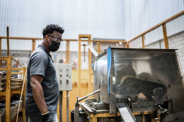 homem adulto médio trabalhando em uma fábrica - usando uma máscara facial - african descent factory accuracy analyzing - fotografias e filmes do acervo