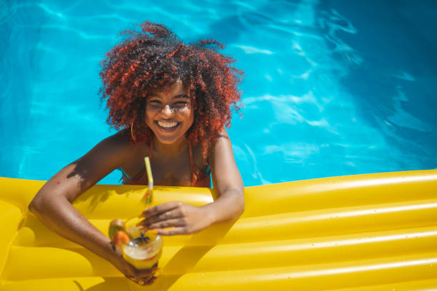 woman floating in swimming pool with tropical cocktail - red hair hairstyle dyed hair women imagens e fotografias de stock