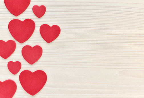 Closeup of red felt hearts on whitewashed wood.