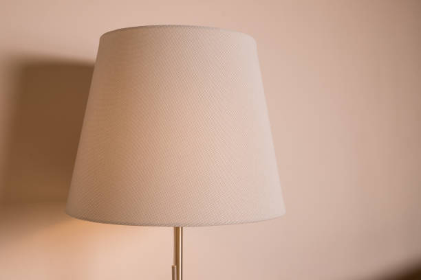 istock Stylish floor lamp on pastel wall background. Idea for interior design. Warm standard lamp, standing lamp.Lamp with a beige shade glowing with cosy golden light. Copy space 1363141467