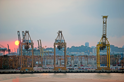 Sunset behind three gantry cranes on Singapore harbour quayside, Singapore, Southeast Asia. Founded by Sir Stamford raffles in 1819 as a trading post of the British Empire, Singapore is now a sovereign state and an important transit point and trading hub for freight, commerce and financial transactions worldwide, as one of the four Asian Tigers trading partners.