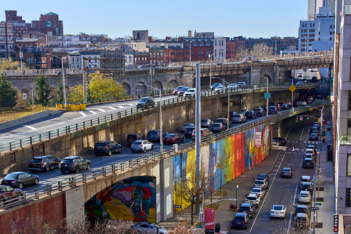 Brooklyn, NY - December 12, 2021: A colorful mural is painted on a retaining wall of the Brooklyn-Queens Expressway (BQE) in DUMBO, Brooklyn, NYC. Beyond the highway traffic is the background is the entrance to the Brooklyn Bridge and Brooklyn Heights