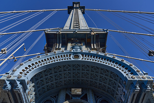 New York, NY - December 12, 2021: Upward view of a tower of the Manhattan Bridge (1909) with beautiful curved steel decorations and a riveted steel tower which is painted blue, seen against a clear blue sky.