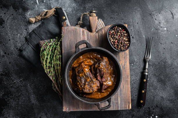 bochechas de carne ensopada com molho de vinho tinto marrom na frigideira. fundo preto. vista superior - veal wine food dinner - fotografias e filmes do acervo