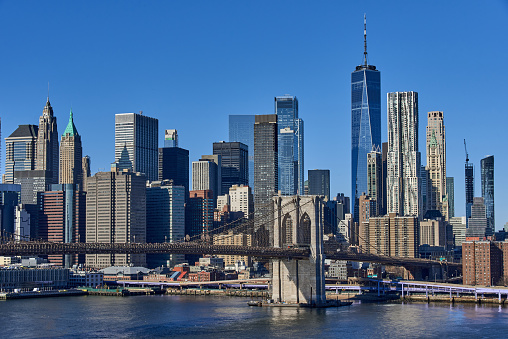 An elevated view of Brooklyn bridge with the skyscrapers of Lower Manhattan and the World Trade Center in the background on a clear cloudless winter day. In the foreground is the East River