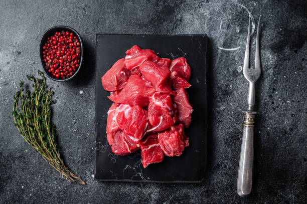 istock Raw diced red beef meat for Goulash on marble board. Black background. Top view 1363145423