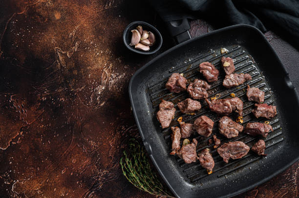 istock Diced beef cubes roasting in a grill pan for stew or goulash. Dark background. Top view. Copy space 1363146318