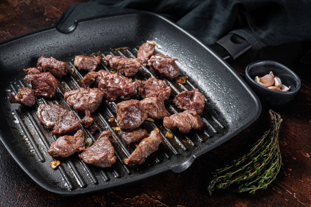 Diced beef cubes roasting in a grill pan for stew or goulash. Dark background. Top view