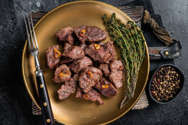 istock Chopped Grilled Diced Beef garlic steak on a plate with thyme. Black background. Top view 1363146344