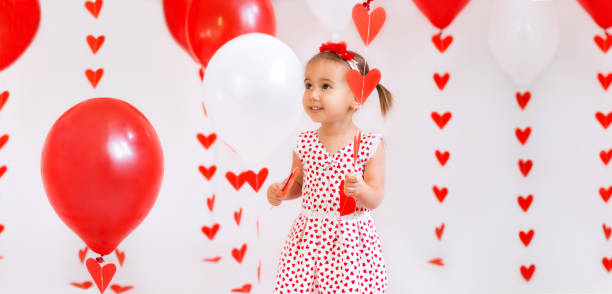 garota com balões e um pirulito em forma de coração parece pensativamente de lado - child valentines day candy eating - fotografias e filmes do acervo