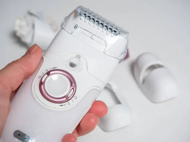 Photo of an electric epilator in a woman's hand.In the background, the various nozzles are out of focus. Devices for women's beauty