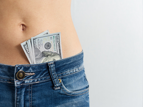 a woman in jeans with a bare stomach with dollars sticking out of her pants. The concept of Striptease.