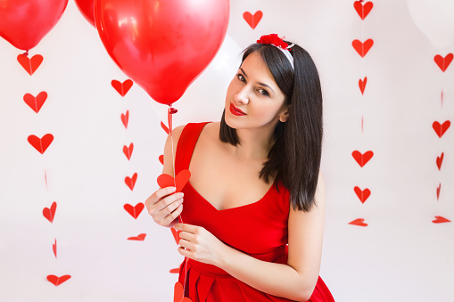Beautiful girl with red balloons and garland-heart. Portrait of a dark-haired girl with red lipstick. Celebrate Valentine's Day.
