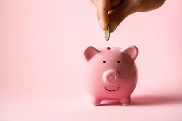 Photo of Hand puts a coin in a piggy bank.