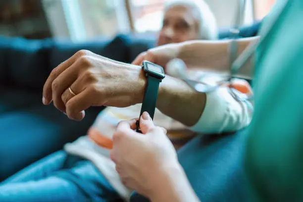 Photo of Smartwatch for assisted living. A woman from the medical health system wears a smartwatch for remote monitoring of vital signs on an elderly person