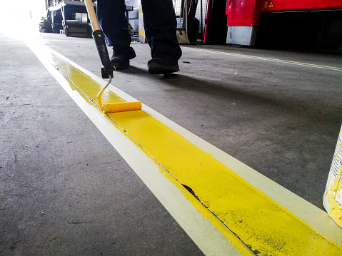 Primer plano de una persona pintando una línea amarilla en el piso de un garaje bajo las luces photo