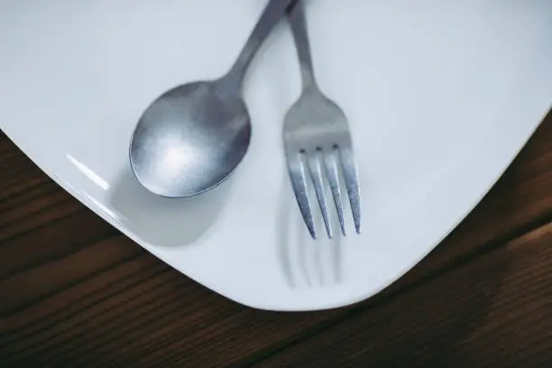 White plate and fork and spoon placed on wooden table