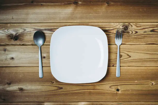 White plate and fork and spoon placed on wooden table