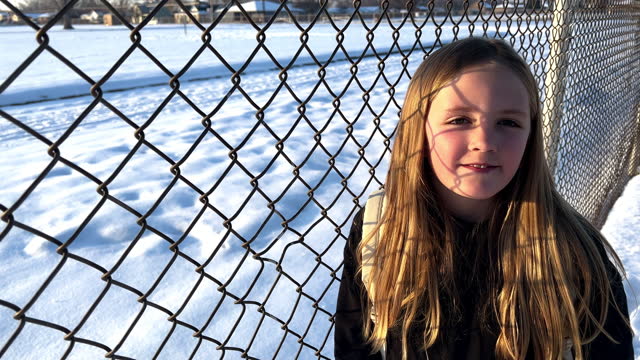 Young girl standing and smiling next to chainlink fence