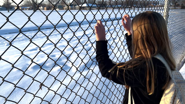 Young girl holding onto chainlink fence and looking around
