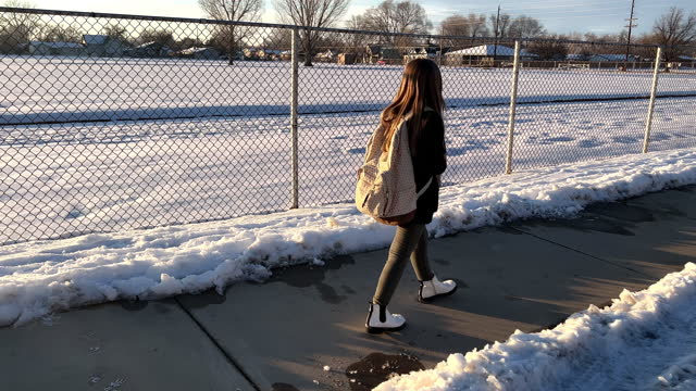 Young beautiful girl walking down sidewalk next to chainlink fence in the winter