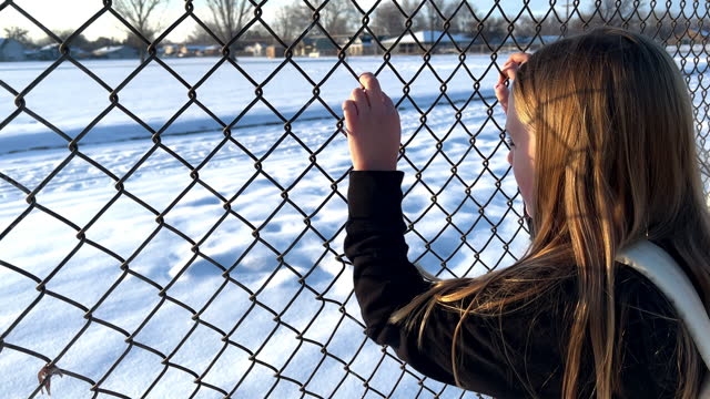 Young girl looking through a chain link fence at a school