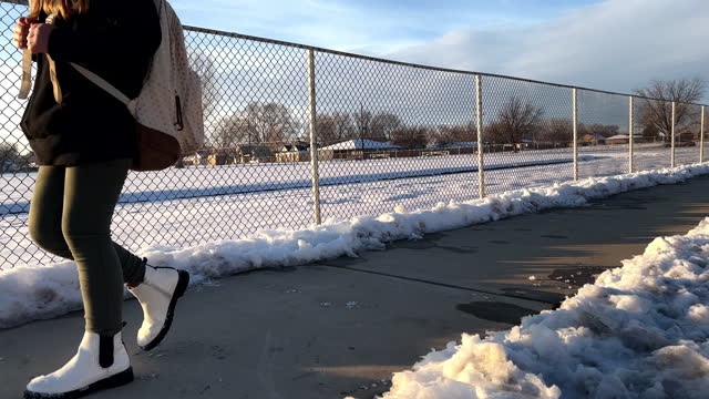 Girl walking by chain link fence near school football field