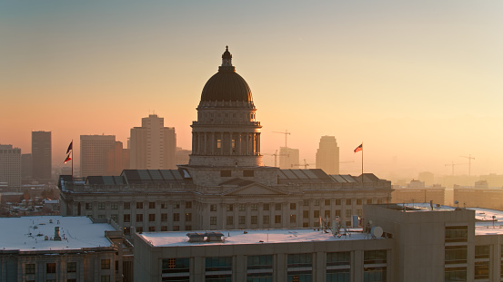 Drone shot of the Utah State Capitol in Salt Lake City on a cold evening in December, with the downtown buildings in the background. The air quality is visibly poor, with smog hanging in the air. \n\nAuthorization was obtained from the FAA for this operation in restricted airspace.