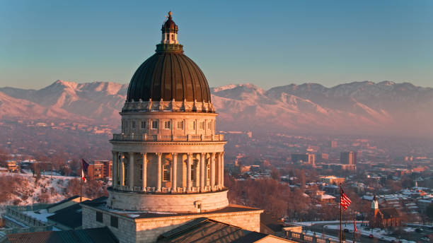 Drone shot of the Utah State Capitol in Salt Lake City on a cold evening in December, with snow on the ground and on the Wasatch Mountains in the distance. The air quality is visibly poor, with smog hanging in the air. \n\nAuthorization was obtained from the FAA for this operation in restricted airspace.