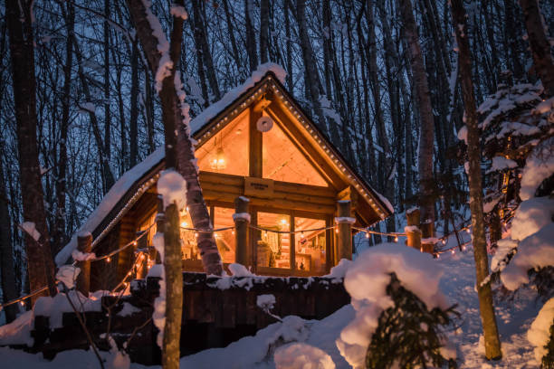 la luce di notte di una piccola casa con neve coperta di neve a ningle terrace a furano, hokkaido, giappone. - mountain chalet foto e immagini stock