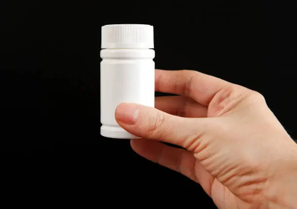 Person hold White Bottle of the Medical Product on the Black Background