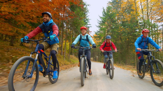 Wide tracking shot of two young women and two men riding mountain bikes on a gravel road through the forest and having fun. Shot in Slovenia.