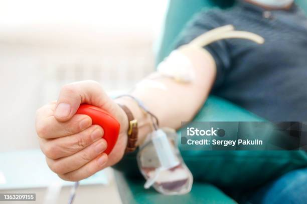 Topic Of Donation Man Donates Blood In Hospital Mans Hand Squeezes Rubber Heart Closeup Donor Sits In Chair Stock Photo - Download Image Now