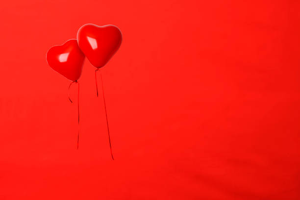 Two red heart shaped balloons floating in mid-air against red background with copy space.
