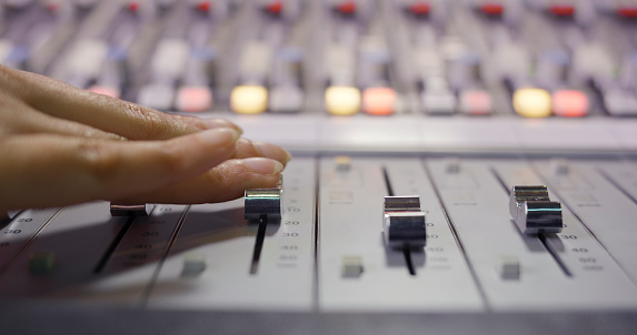 Close-up of human hand adjusting buttons on audio mixer in recording studio.