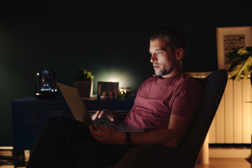Worried business man watching or reading something on his laptop while sitting in armchair in a living room.