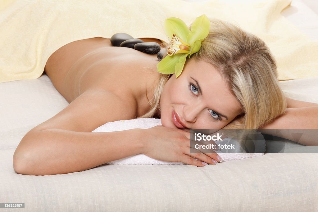 Woman relaxing with flower and hot stones Young woman relaxing on the bed with flower and hot stones 20-24 Years Stock Photo